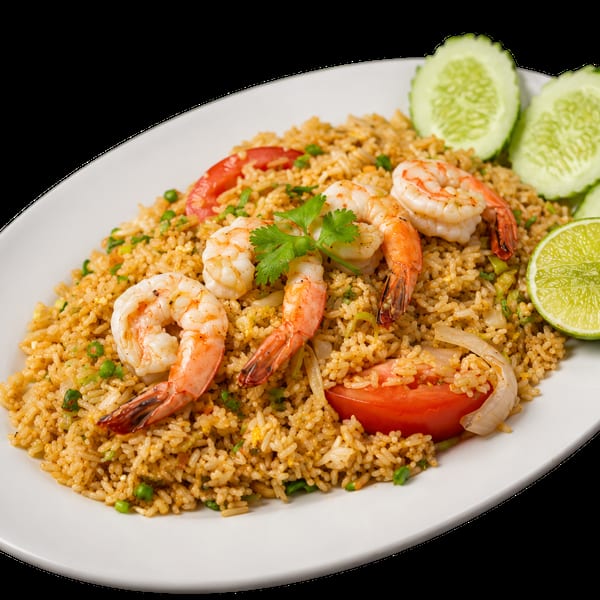 Shrimp fried rice with tomatoes, onions, peas, cilantro, lime, and cucumber slices on a white plate.