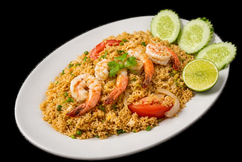 Shrimp fried rice with tomatoes, onions, peas, cilantro, lime, and cucumber slices on a white plate.